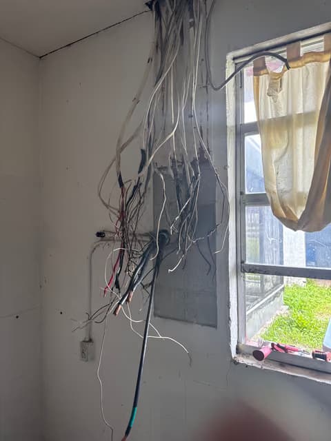 Pared abierta con un manojo de cables eléctricos expuesto cerca de una ventana durante una renovación