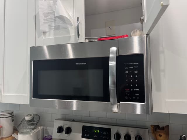 Nuevo microondas de acero inoxidable instalado sobre la estufa en una cocina