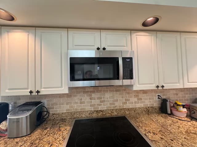 Gabinetes de cocina blancos con un nuevo microondas de acero inoxidable y azulejo decorativo