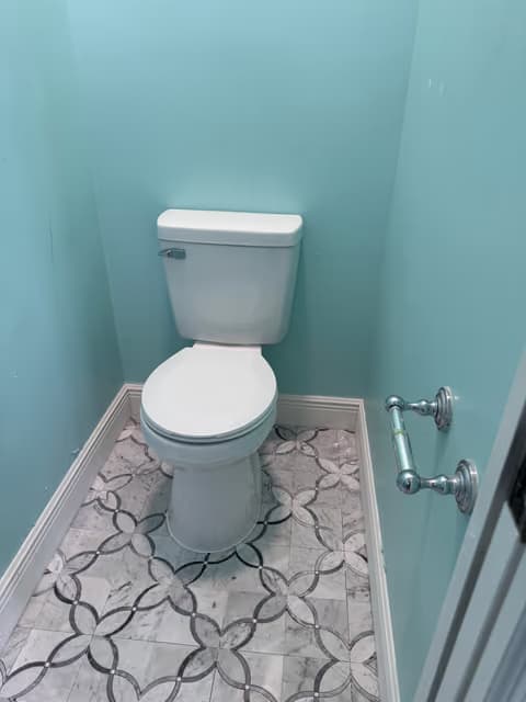 Baño pequeño con un nuevo inodoro, piso de azulejo estampado y paredes color turquesa