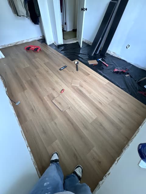 Instalación de piso de madera en progreso con herramientas en el suelo